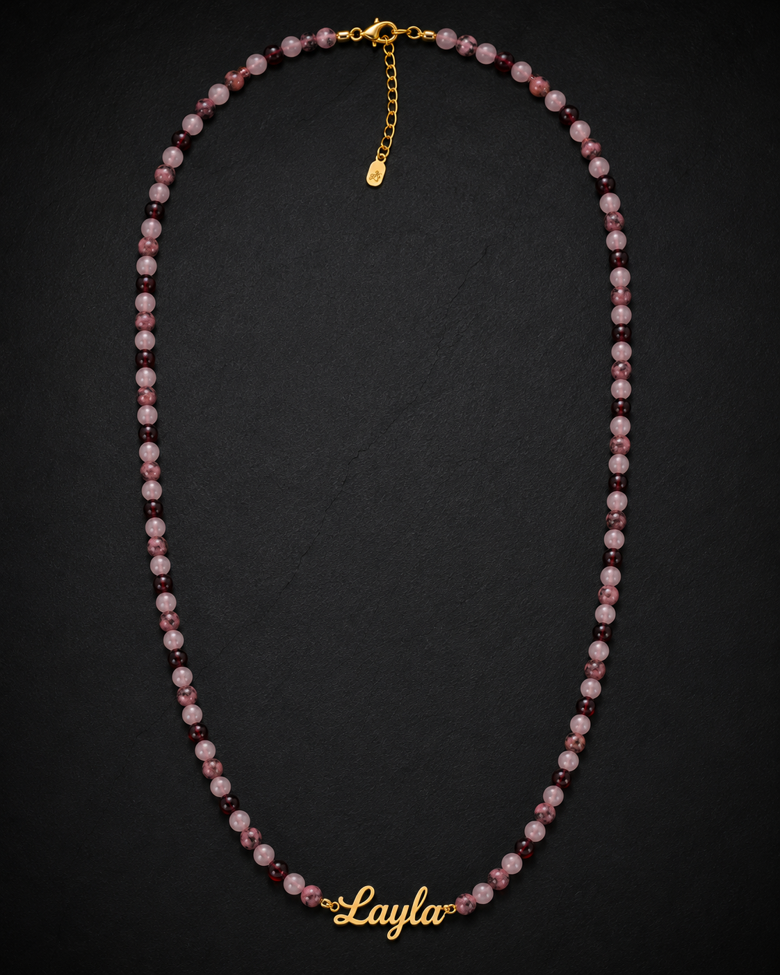 Necklace with pink and purple beads and gold clasp on a dark background
