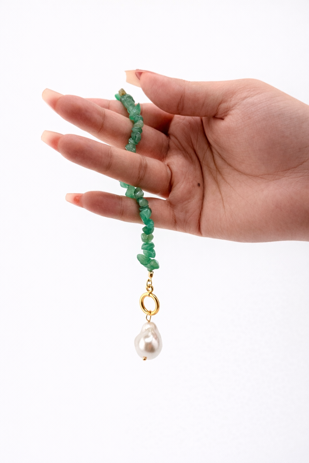 Hand holding a green beaded necklace with a pearl pendant on a white background