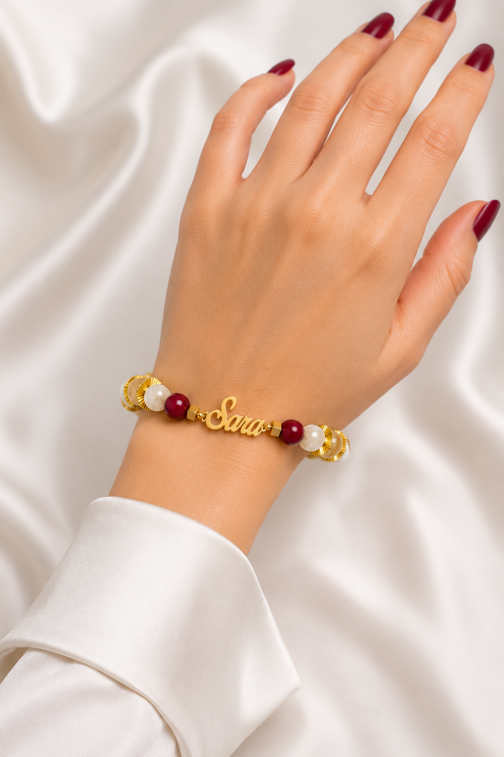 Hand wearing a bracelet with pearls and red beads on a white fabric background