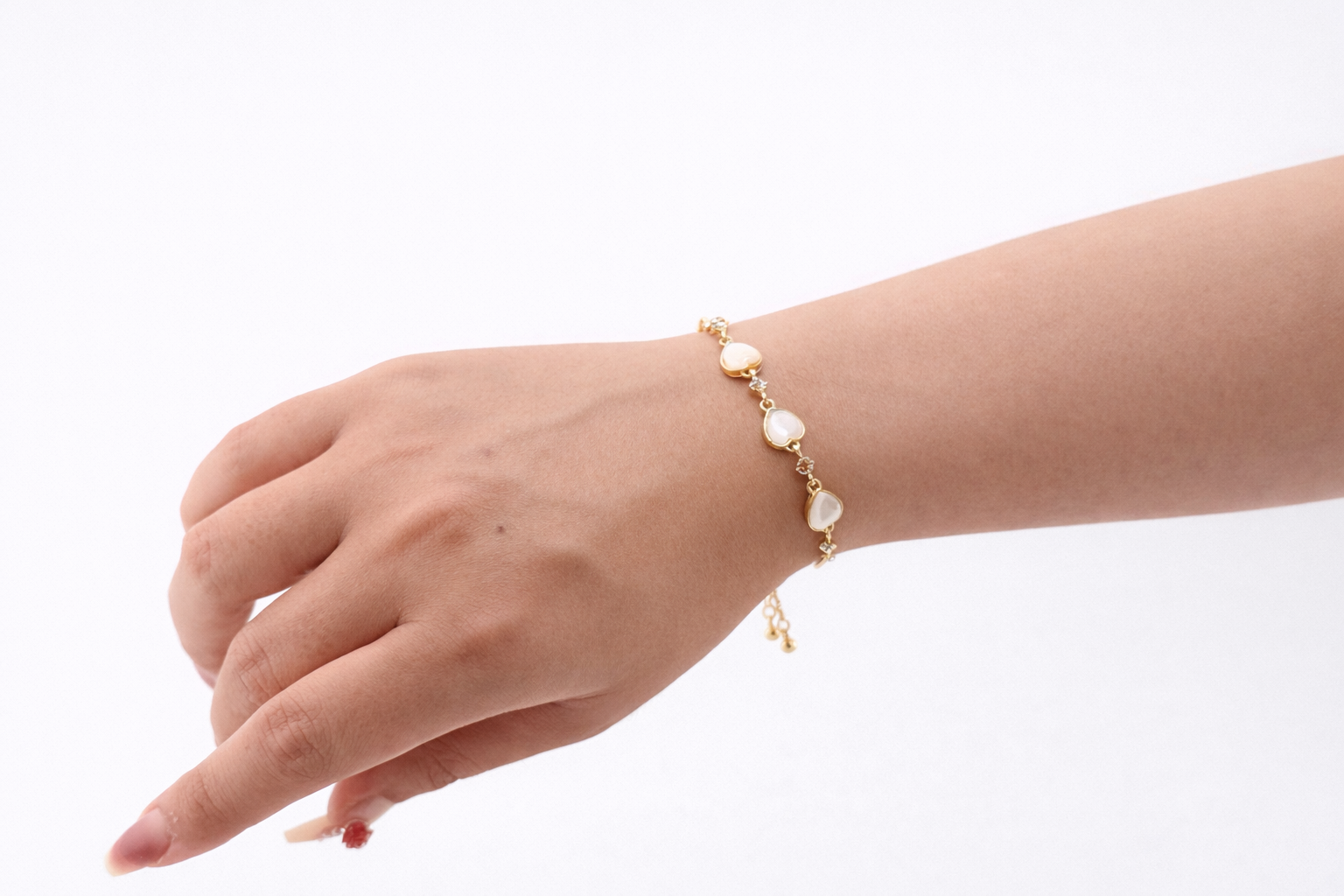 Hand wearing a gold bracelet with pearl-like stones on a white background