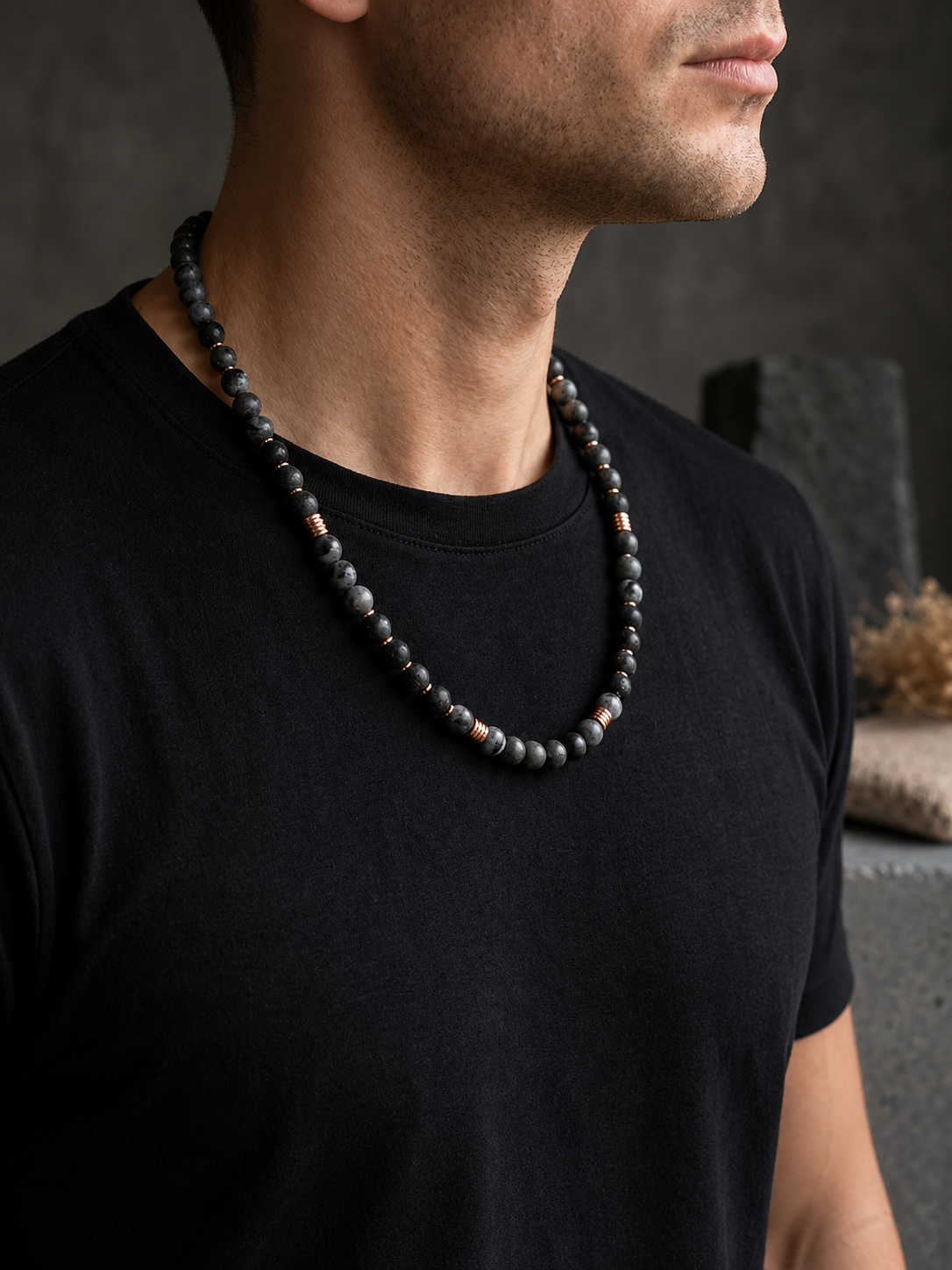 Man wearing a black beaded necklace against a dark background