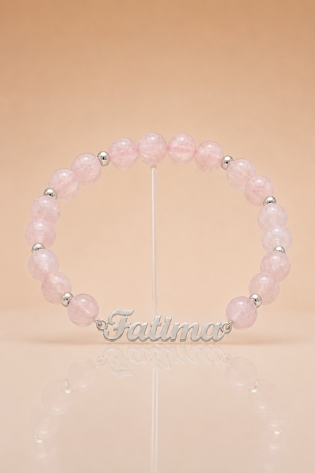 Pink beaded bracelet with silver name charm on a beige background