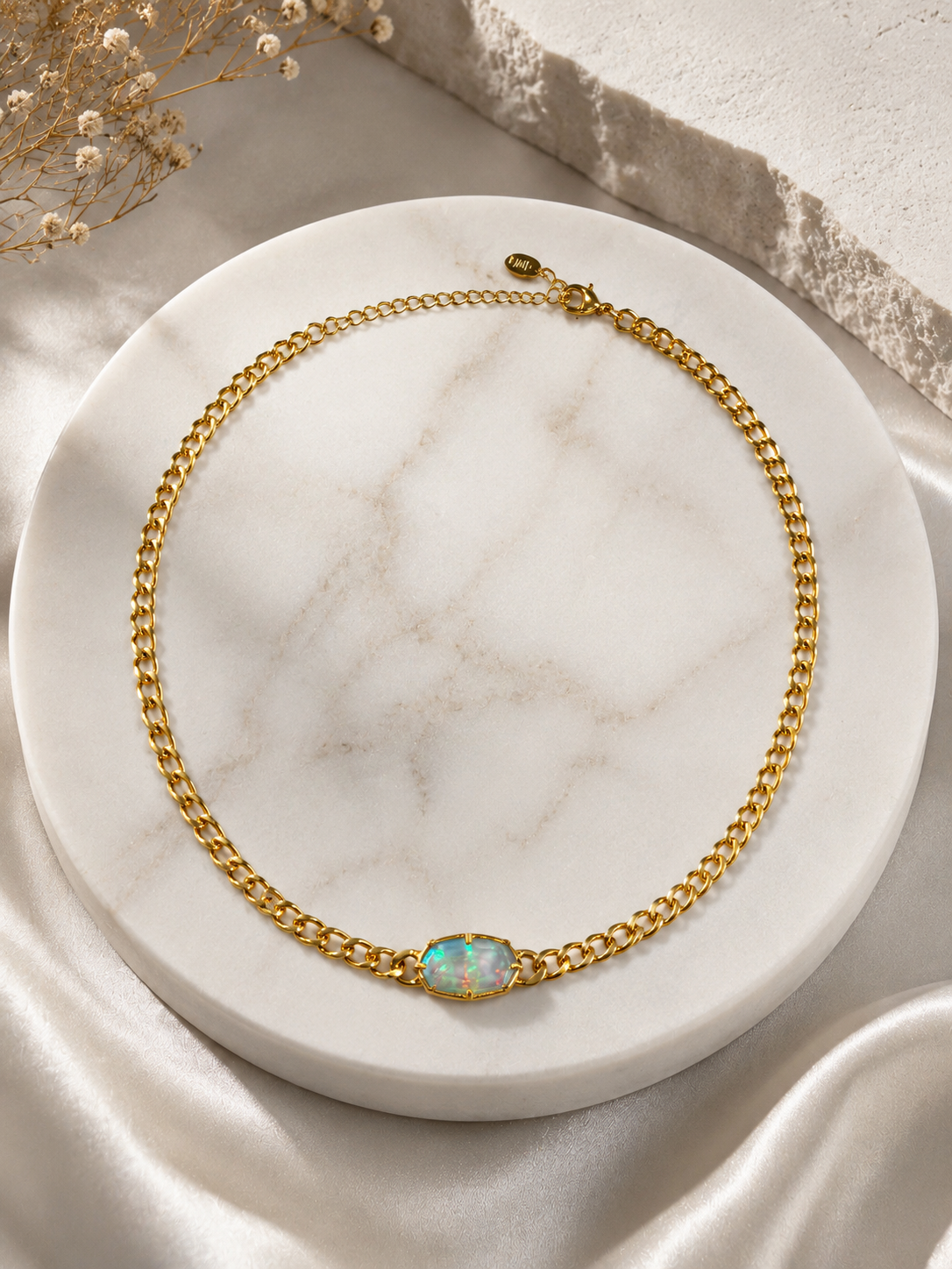 Gold chain necklace with an opal pendant on a marble surface