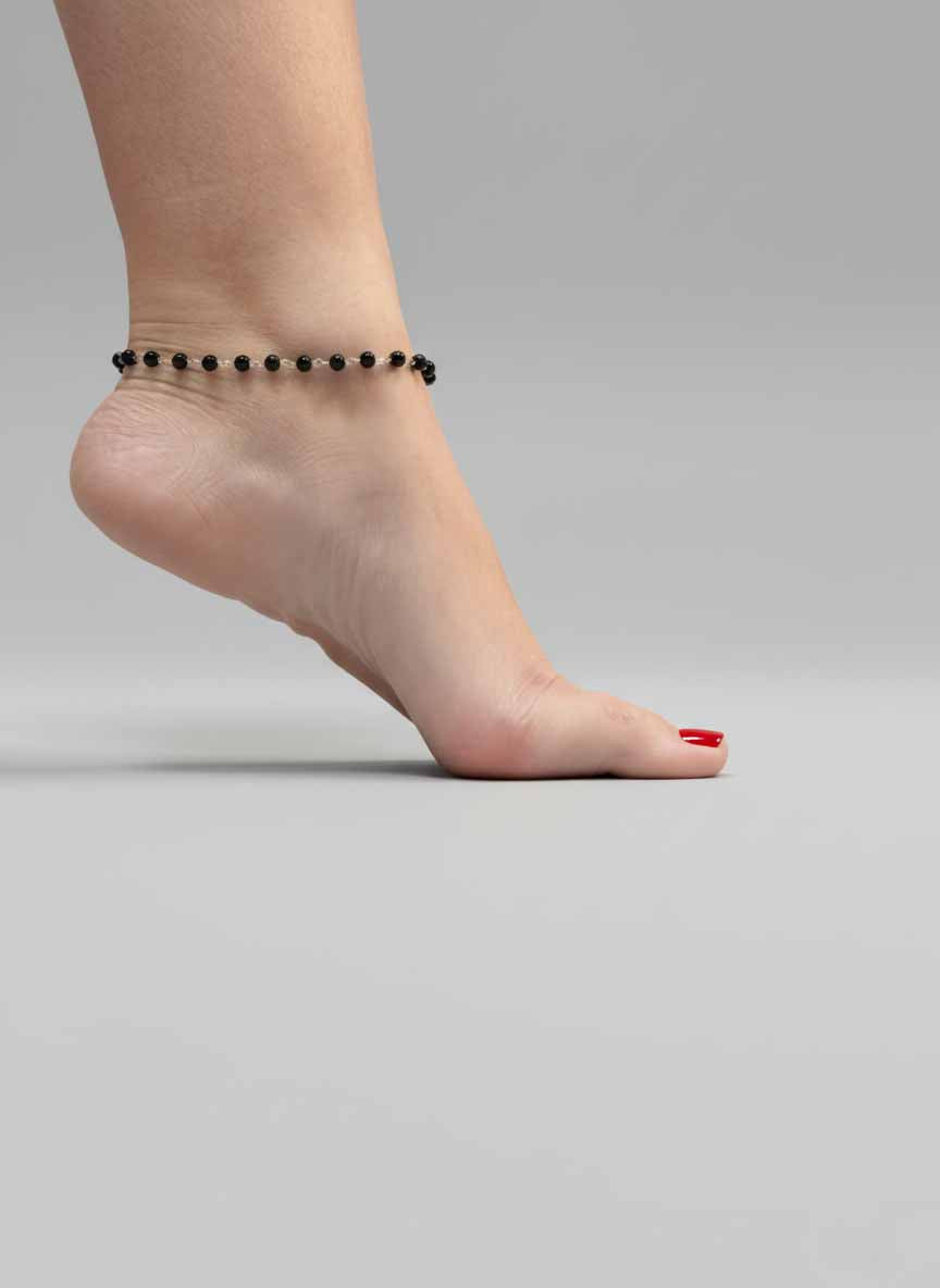 Ankle with a black beaded anklet on a plain background