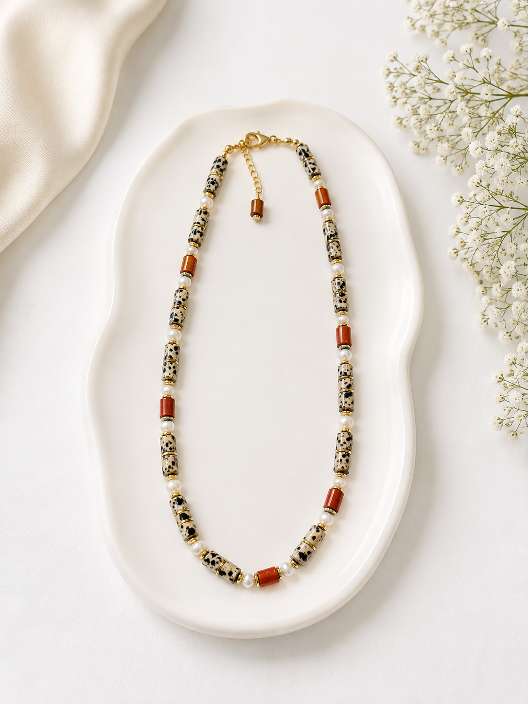 Necklace with multicolored beads on a white dish with flowers in the background