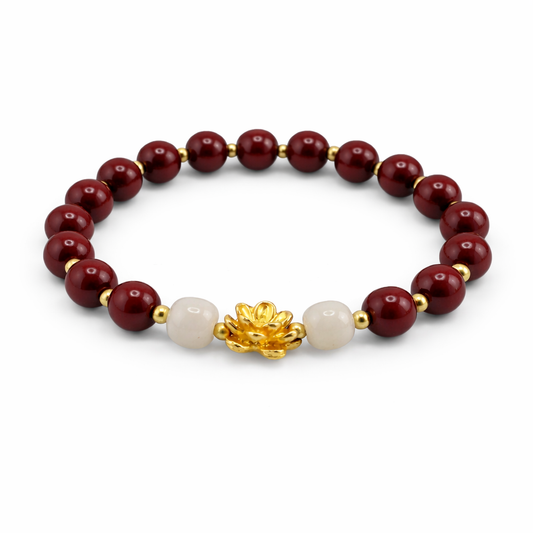 Bracelet with red beads, white pearl, and gold lotus charm on a white background