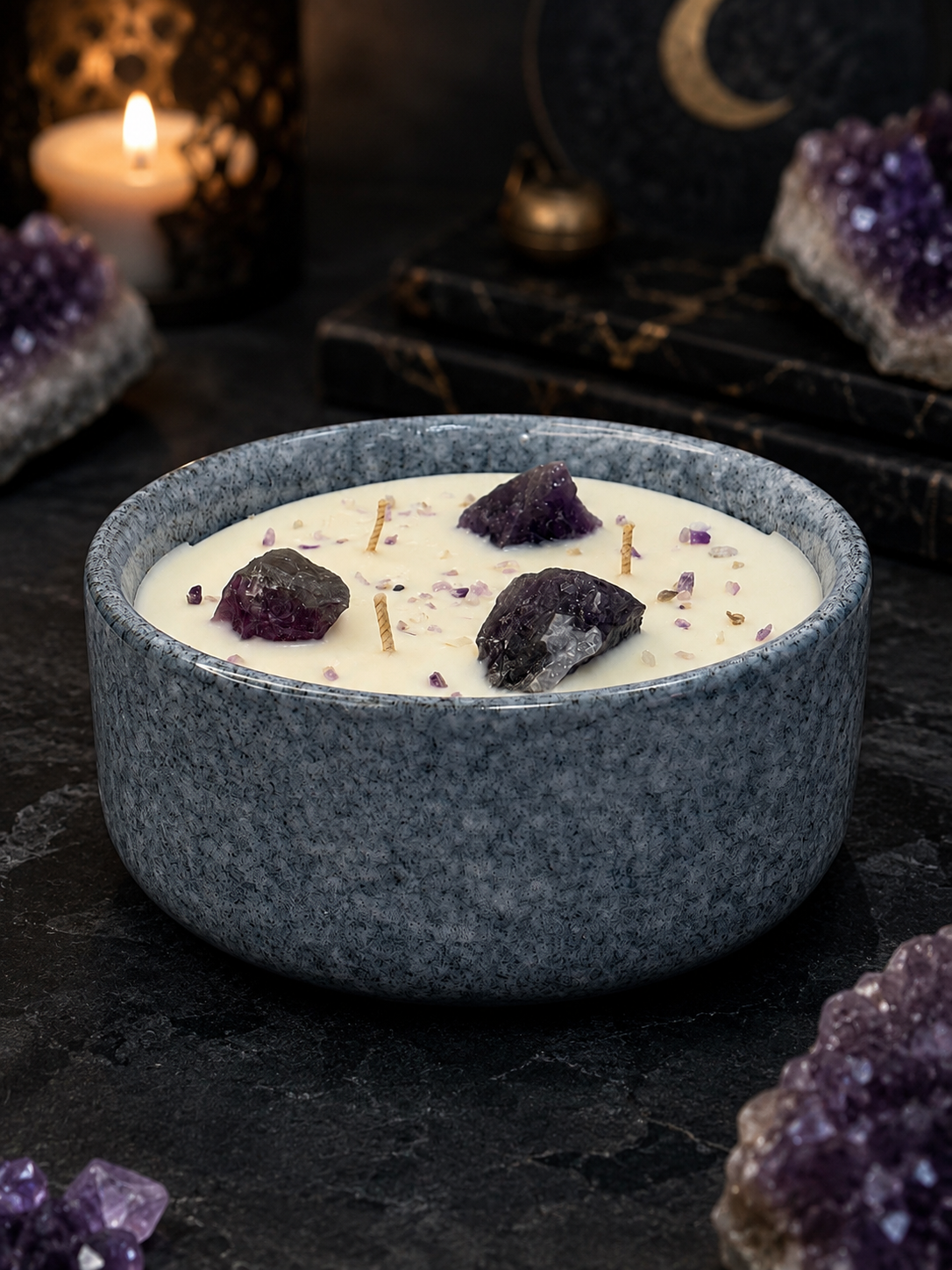 Blue ceramic bowl with a white creamy substance and purple crystals on a dark surface with amethysts and candles.