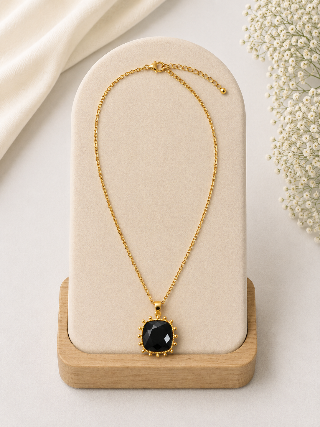 Gold necklace with a black pendant on a beige stand with a light background