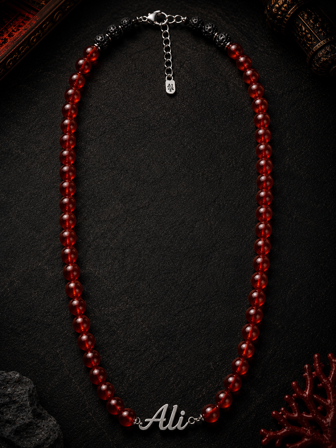 Red beaded necklace on a dark surface with 'Ali' branding.