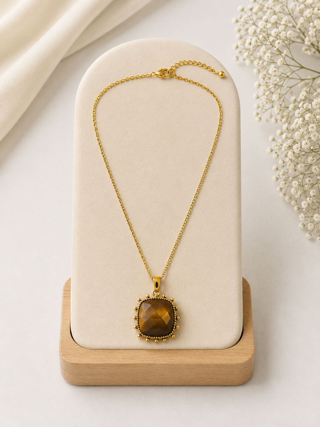 Gold necklace with a brown pendant on a white stand with a light background