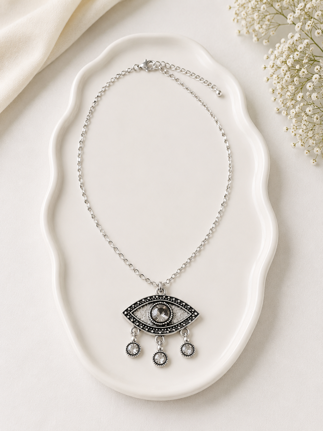Necklace with an eye-shaped pendant on a white dish with flowers in the background