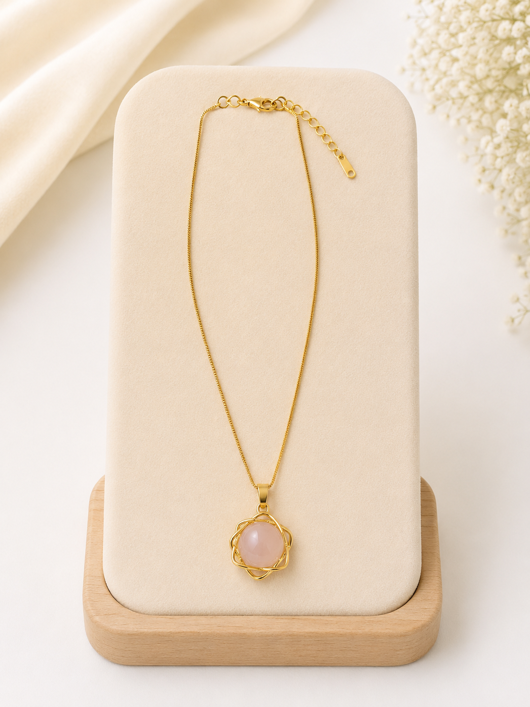 Gold necklace with a pink pendant on a beige stand
