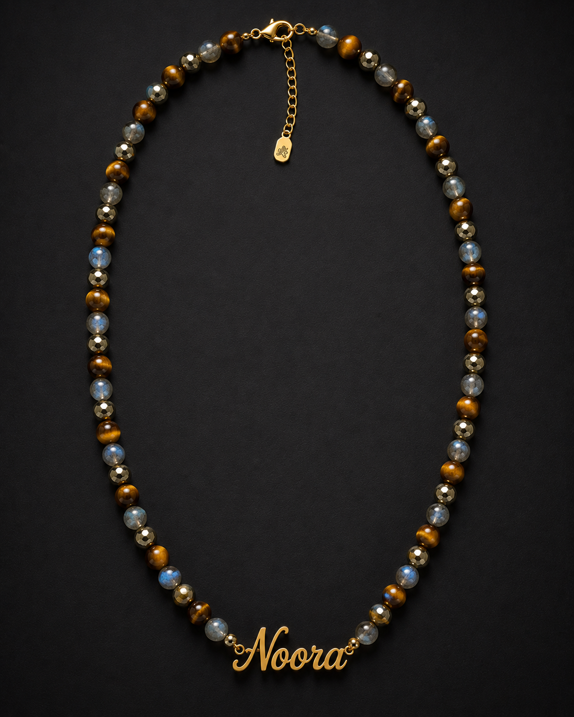 Necklace with beads and a gold 'Noora' charm on a dark background