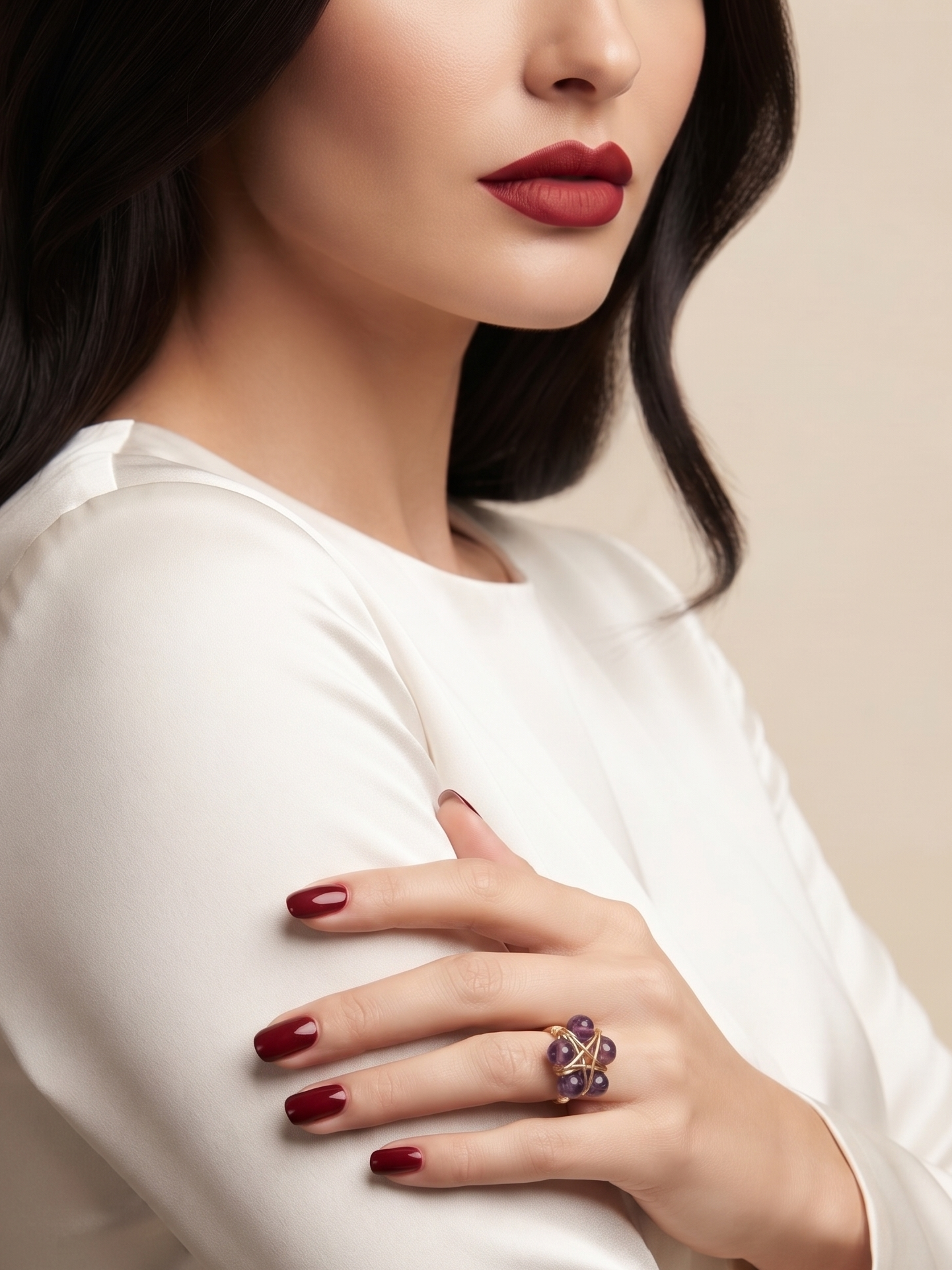 A close-up lifestyle shot of a woman wearing a white satin long-sleeve top and a prominent statement ring on her finger. The ring features a silver-toned band with four large, round, dark purple gemstones.