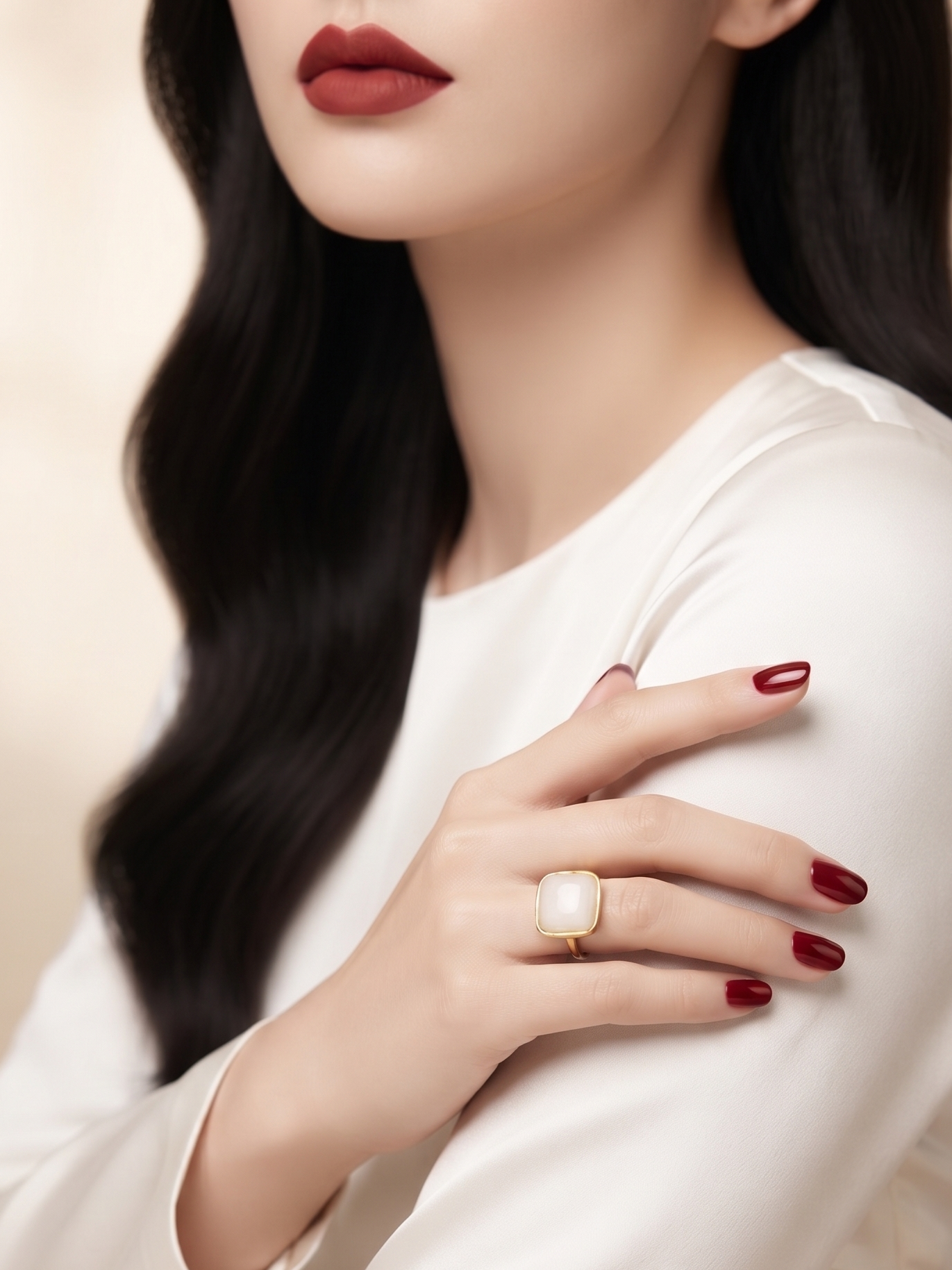 A close-up lifestyle shot of a woman wearing a large rectangular cream-colored ring with a gold band on her finger, paired with a white long-sleeve top and dark red nail polish.