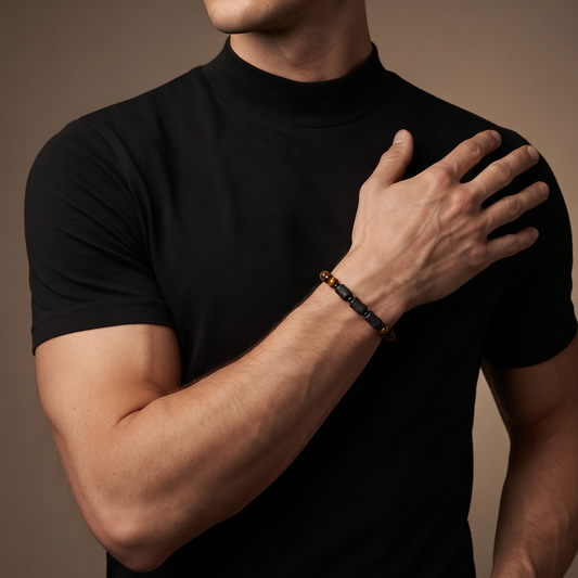 A close-up of a man wearing a black short-sleeve mock neck t-shirt and a dark beaded bracelet on his wrist, posed against a solid warm brown background.