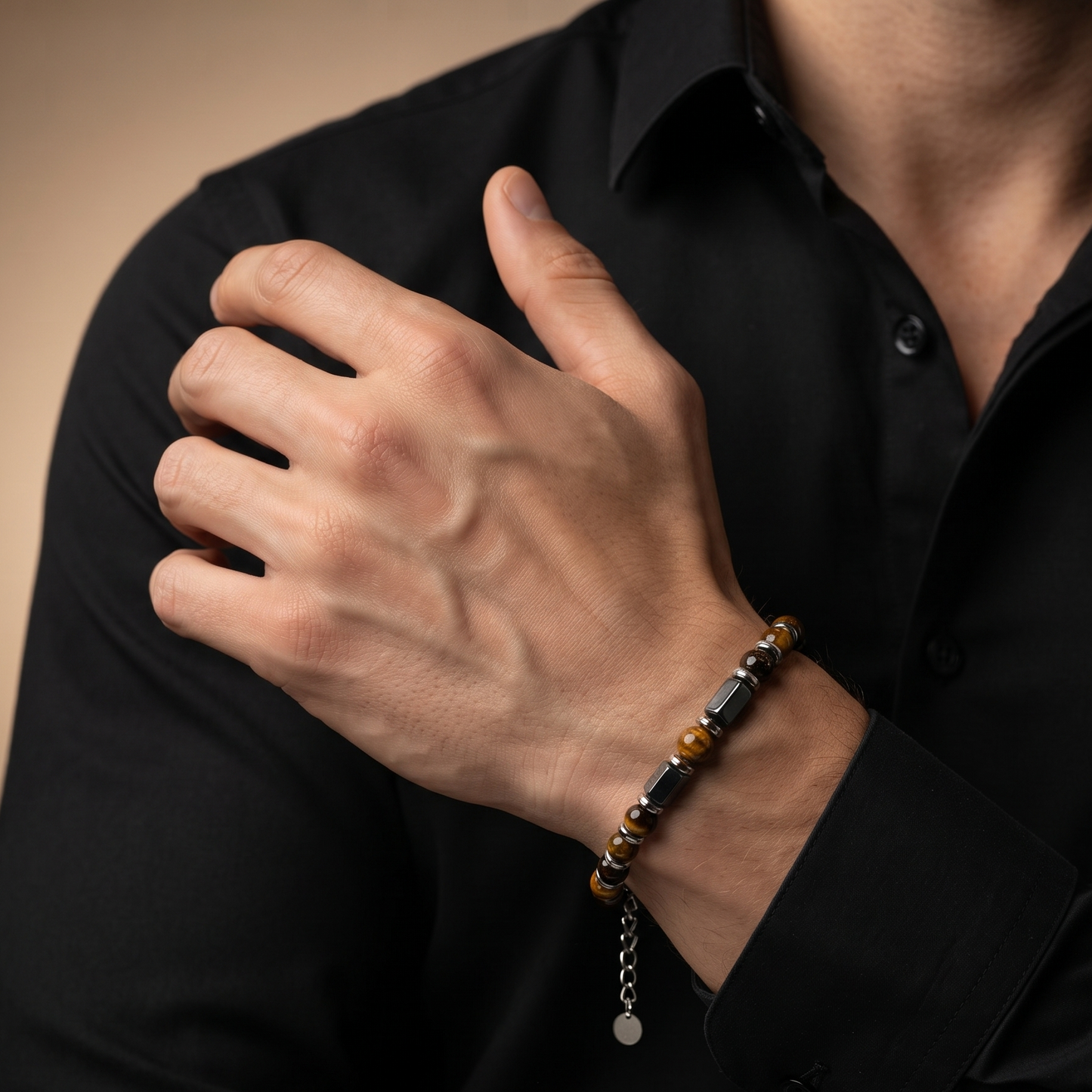 A close-up of a man wearing a black button-down shirt, showcasing a beaded bracelet on his wrist. The bracelet features alternating polished black and tiger's eye beads with a silver-tone chain extender and a small round charm.