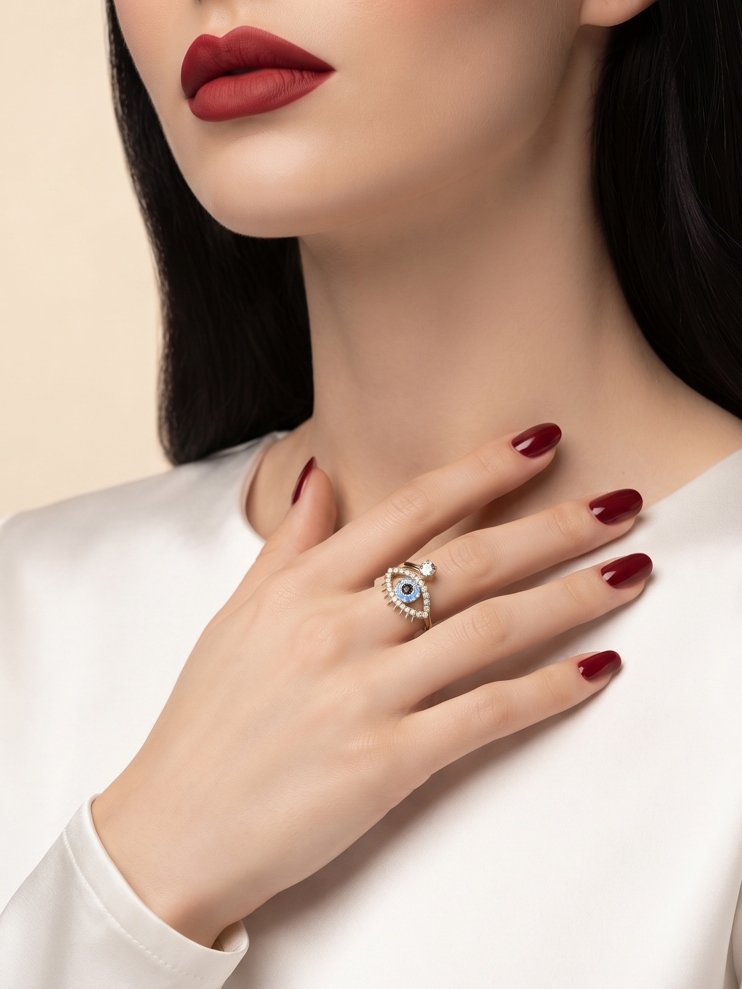 A close-up lifestyle shot of a model wearing a silver eye-of-providence ring with a light blue stone, styled with a white satin top and dark red lipstick.