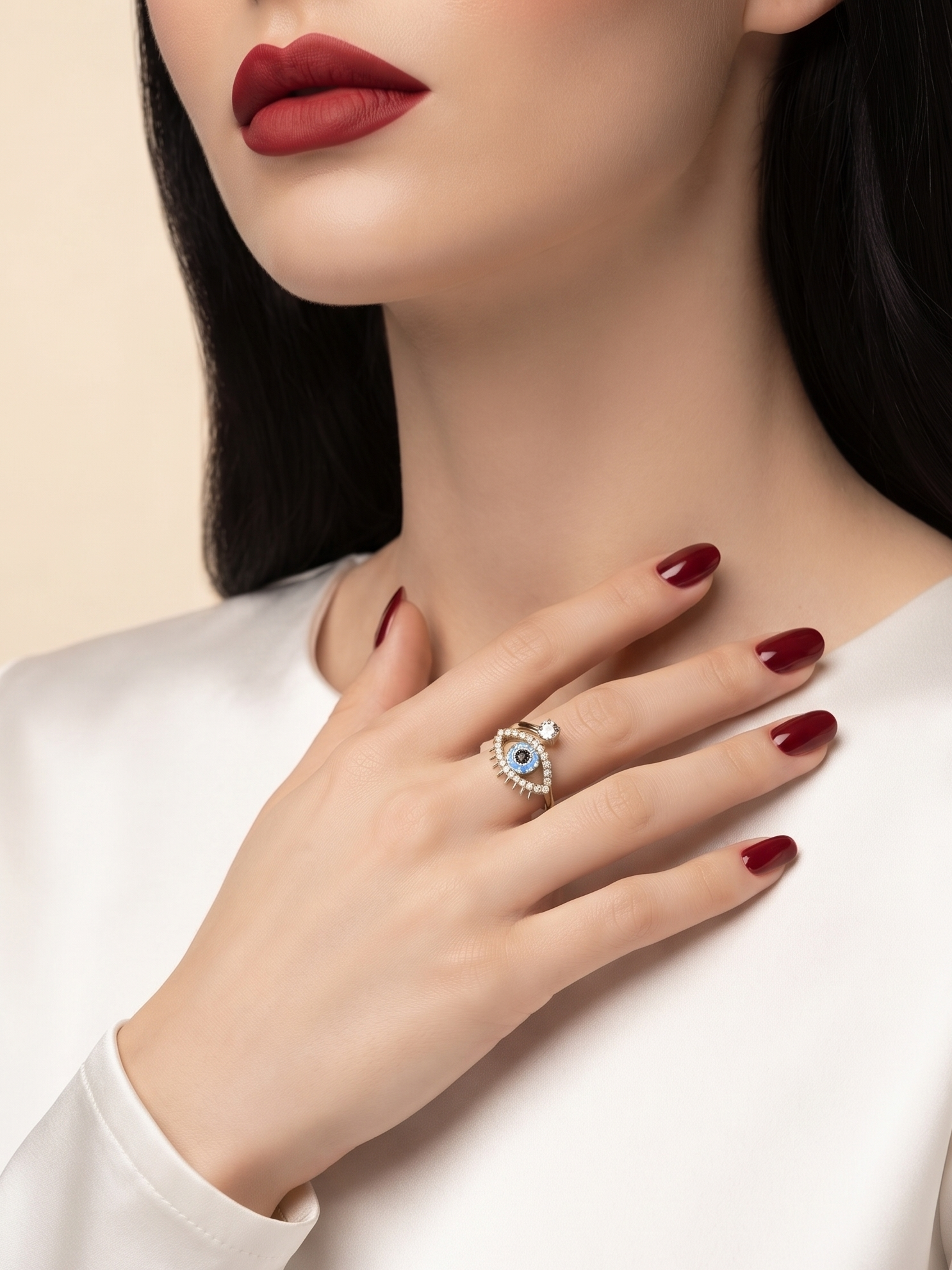 A close-up lifestyle shot of a model wearing a silver eye-of-providence ring with a light blue stone, styled with a white satin top and dark red lipstick.
