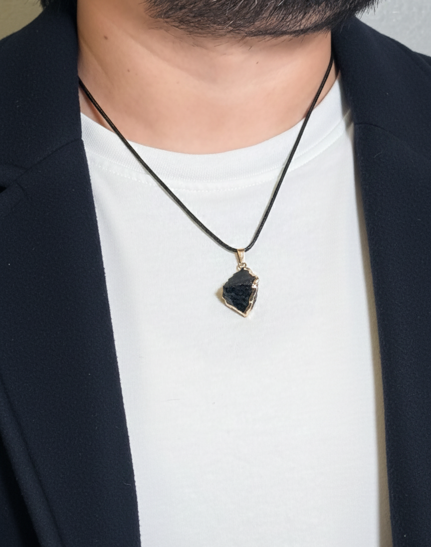Person wearing a black necklace with a pendant on a plain background