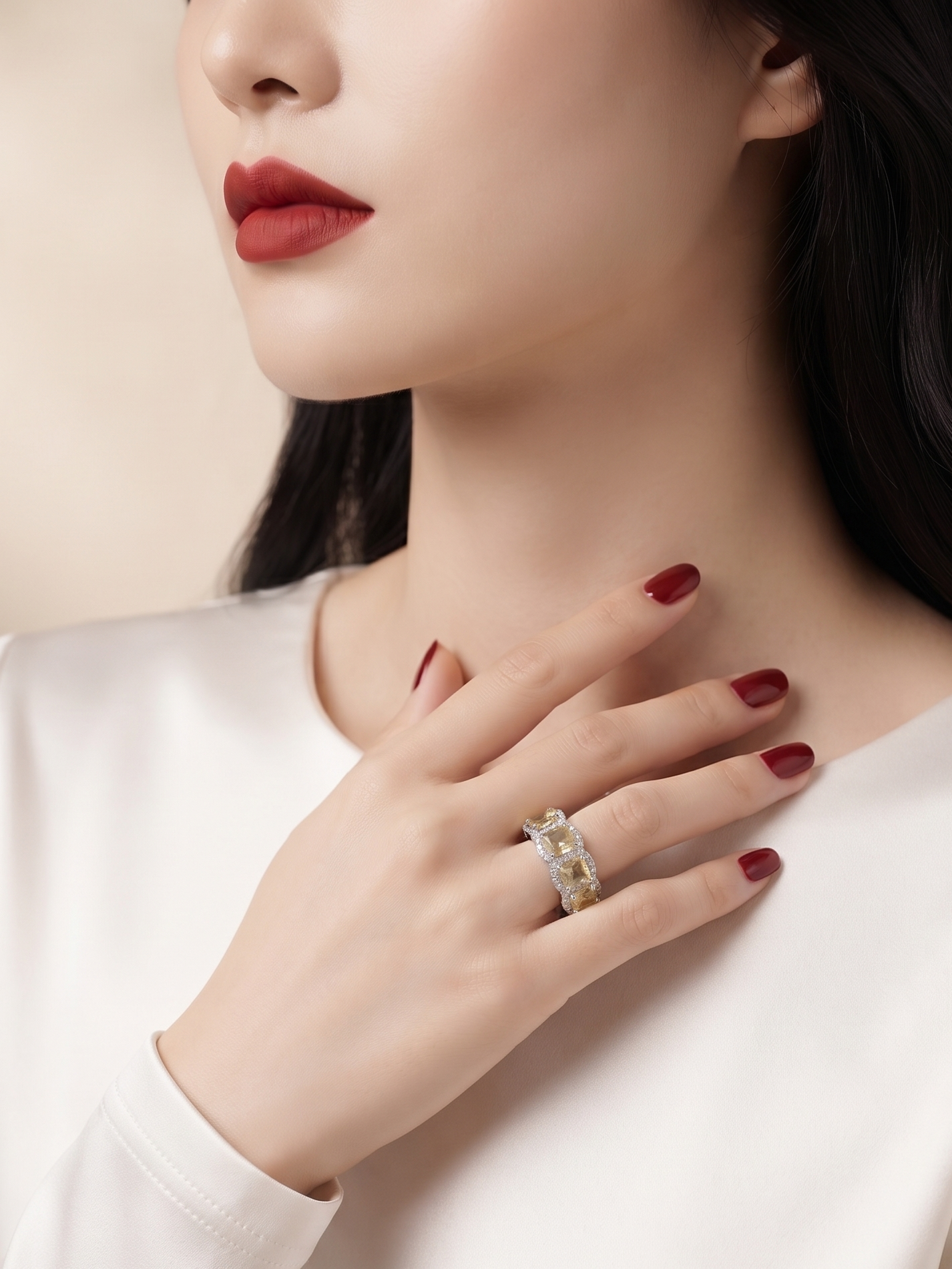 A close-up lifestyle shot of a woman wearing a delicate silver ring with small clear stones on her finger, paired with a white satin top and dark hair.