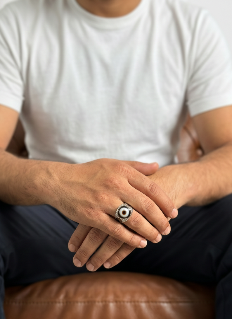 Person wearing a white t-shirt and dark pants sitting on a brown leather couch with hands clasped.