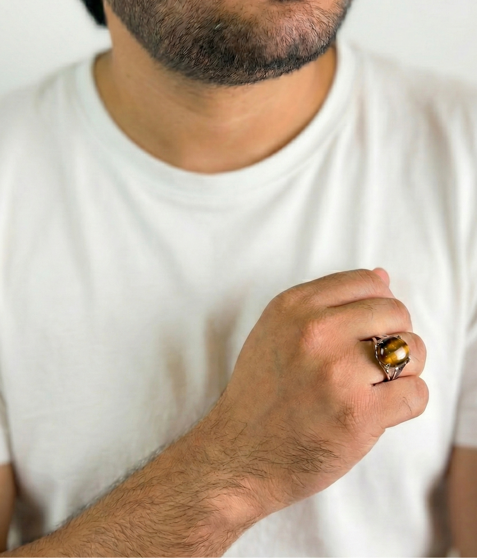 Man wearing a white t-shirt and a ring with a tiger's eye stone.
