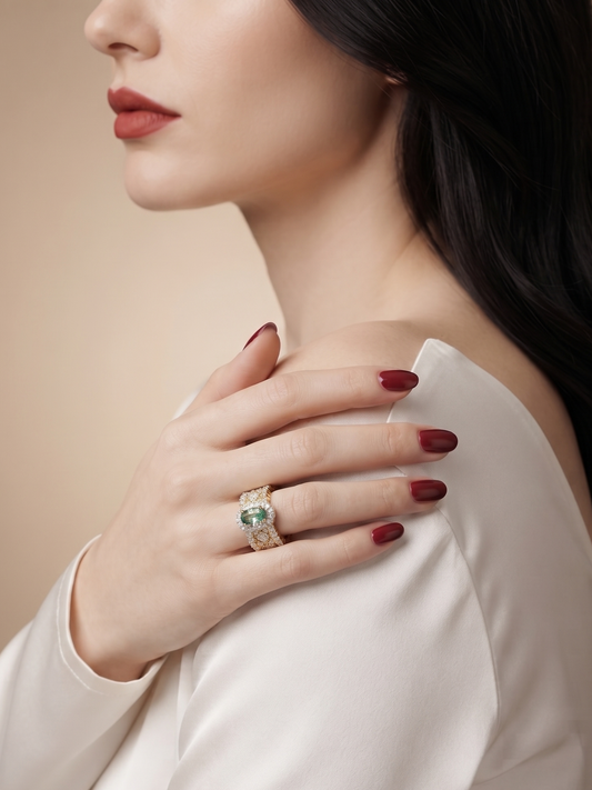 A close-up lifestyle shot of a woman wearing a gold ring with a green emerald-cut center stone, shown on her finger as she rests her hand on her shoulder.