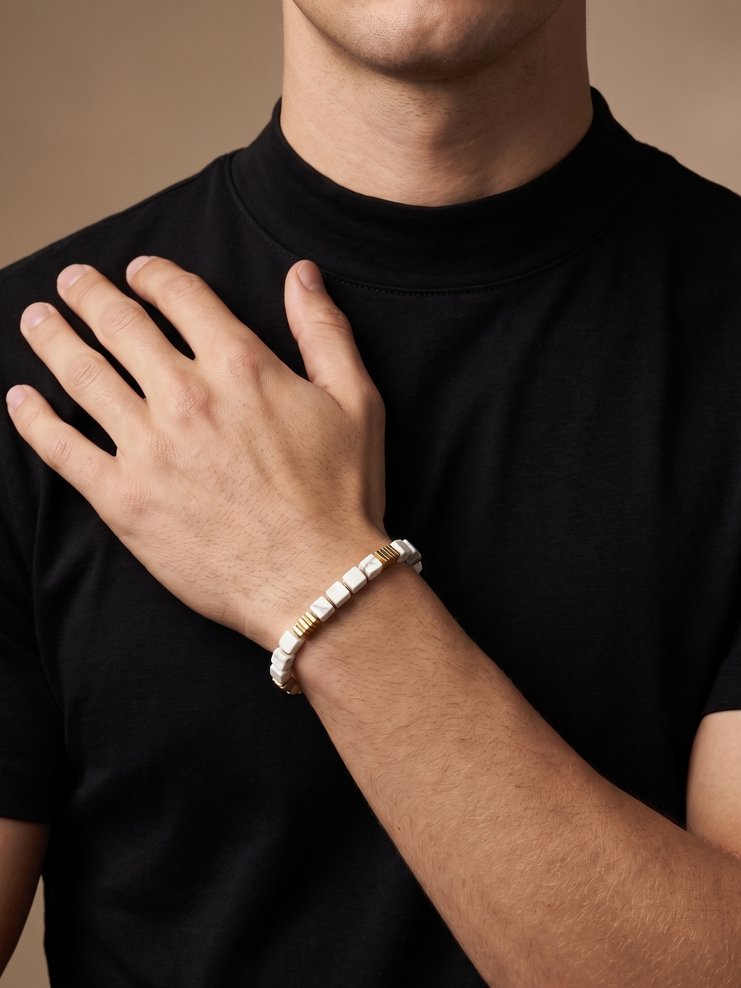 A close-up of a man wearing a black t-shirt and displaying a silver-toned beaded bracelet on his wrist.