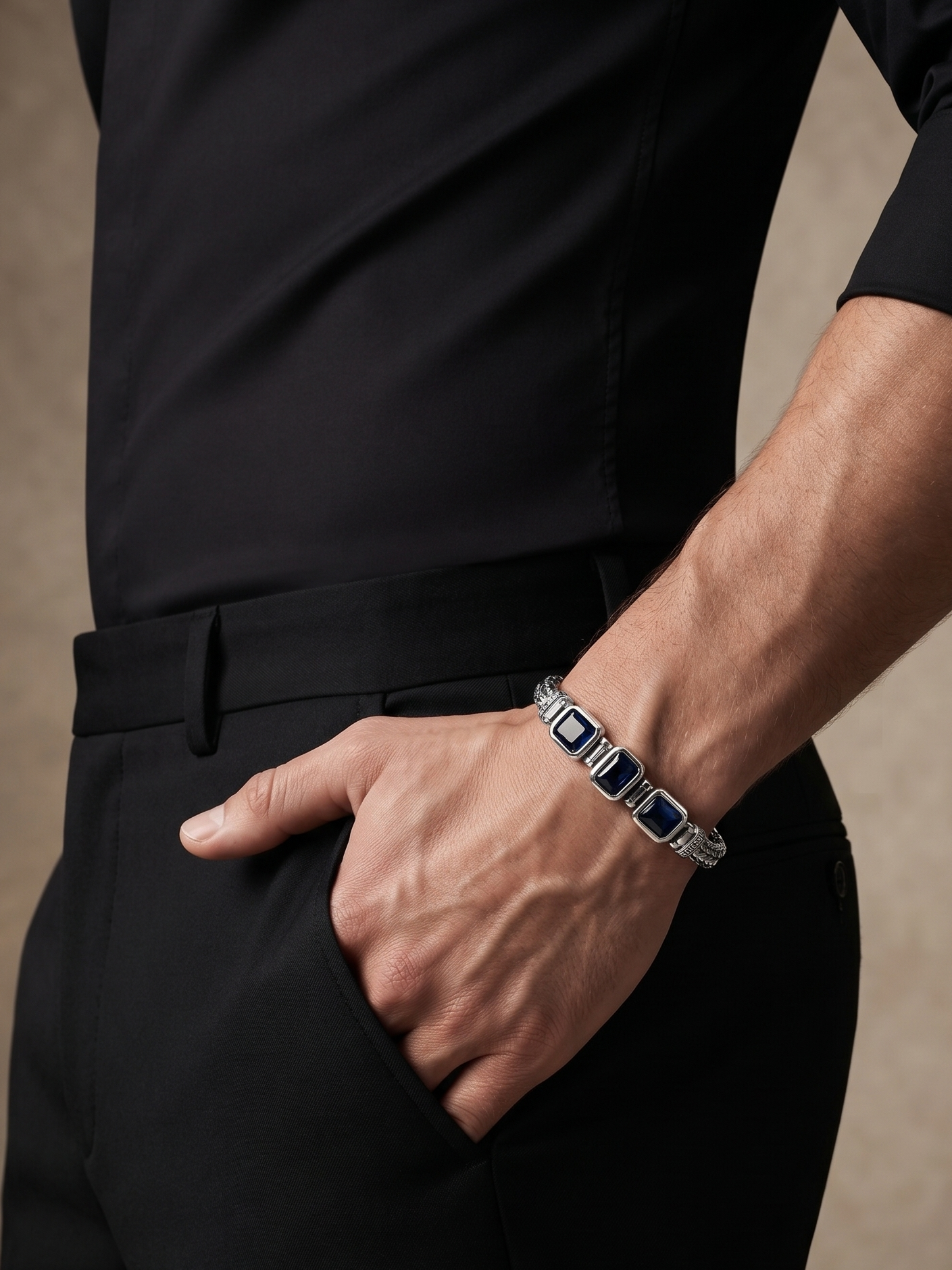 A close-up lifestyle shot of a man wearing a black shirt and trousers, showcasing a silver-toned bracelet with rectangular dark blue inlays on his wrist.