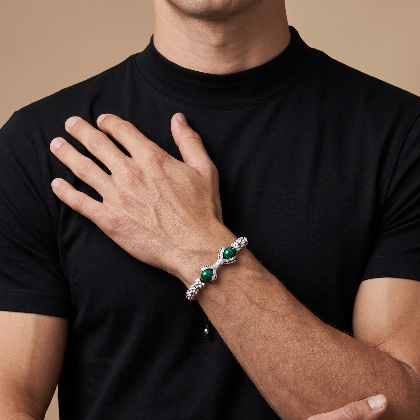 A close-up of a man wearing a black t-shirt and showcasing a silver infinity bracelet with green gemstone accents on his wrist.