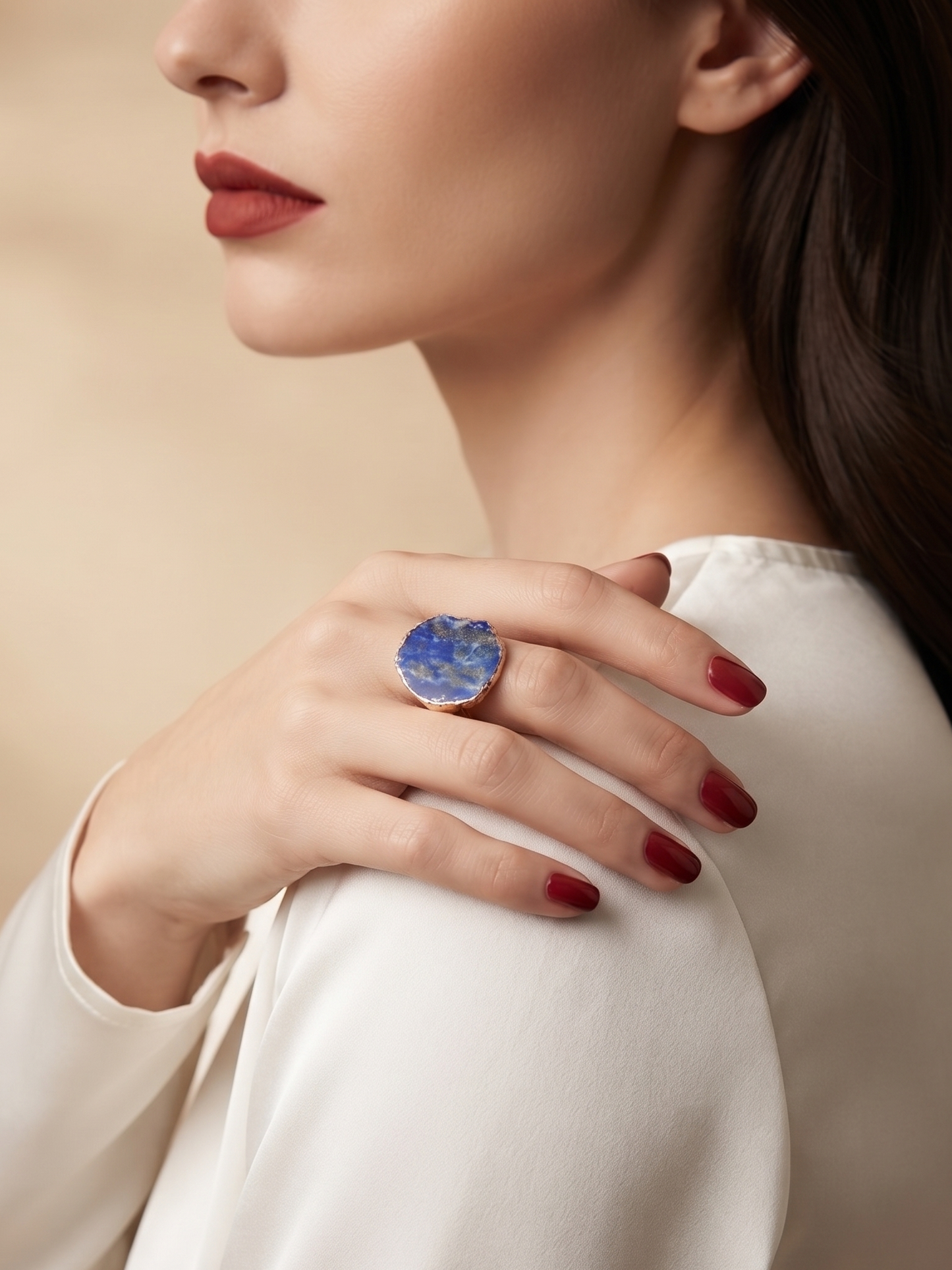 A close-up lifestyle shot of a woman wearing a large round bezel-set ring with a blue marbled stone, shown on her finger as she wears a white satin blouse.