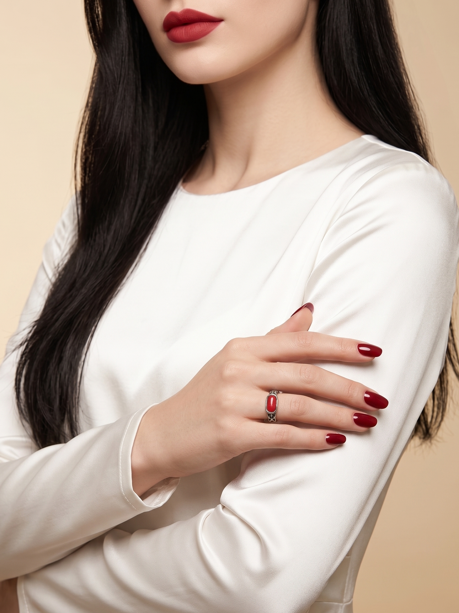 A close-up of a woman wearing a white long-sleeve top, with her arms crossed. She is wearing a silver ring with a red rectangular stone on one finger.