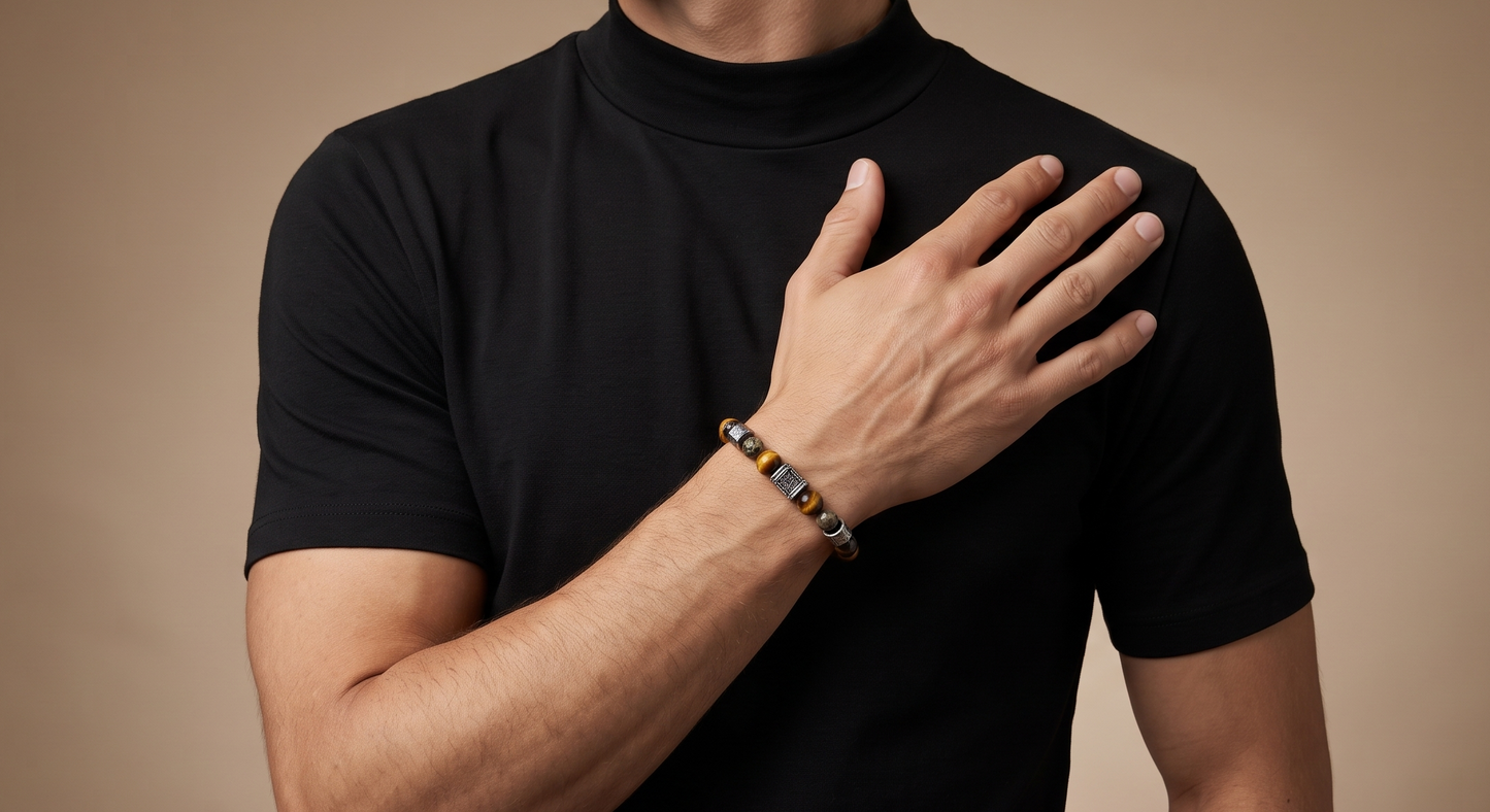A man wearing a black short-sleeve mock neck t-shirt and a beaded bracelet on his wrist, standing against a solid warm brown background.