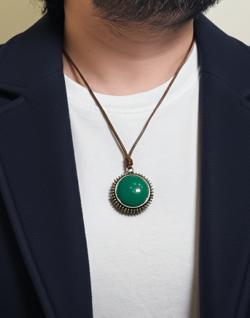 Person wearing a necklace with a green pendant and dark blue blazer