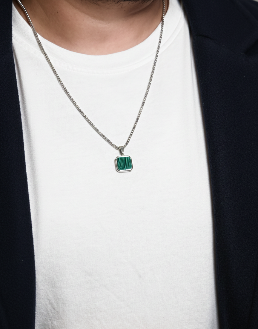 Person wearing a necklace with a green pendant on a white shirt.