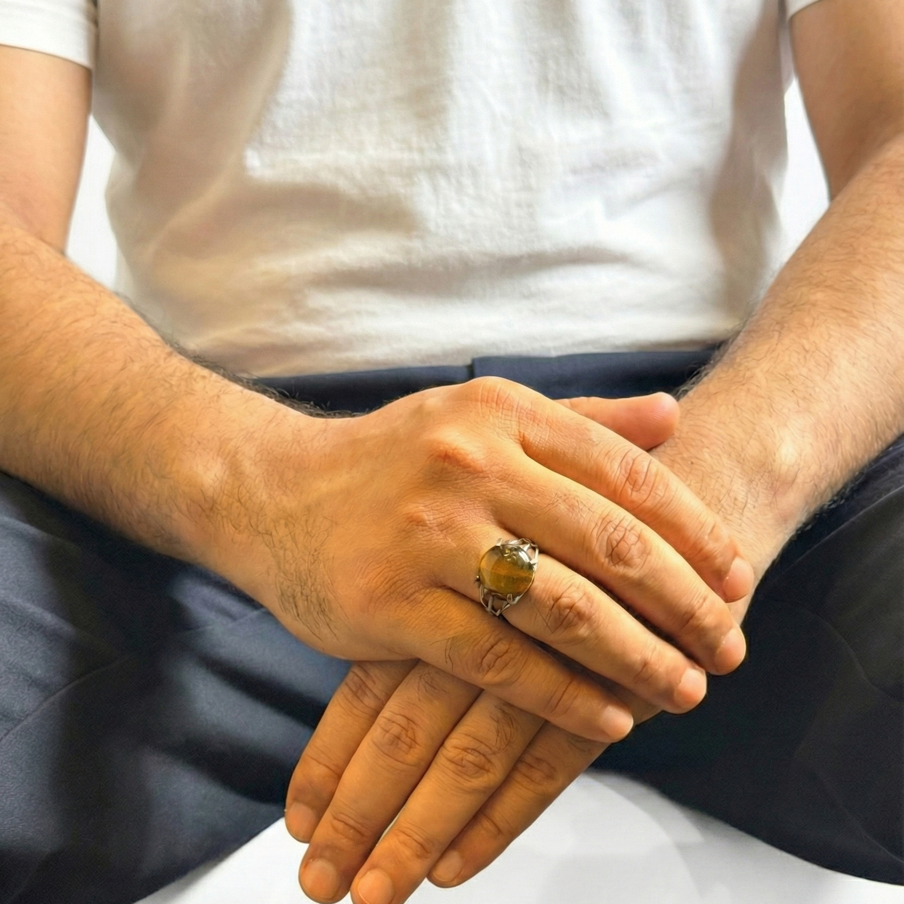 Close-up of hands with a ring, wearing a white shirt and dark pants.