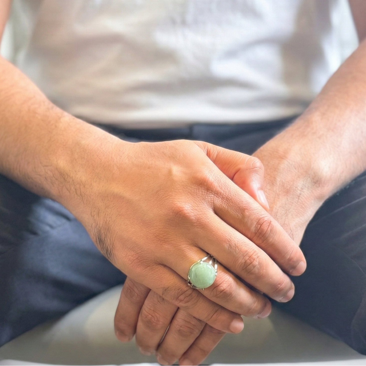 Person wearing a green ring with hands clasped together on a blurred background