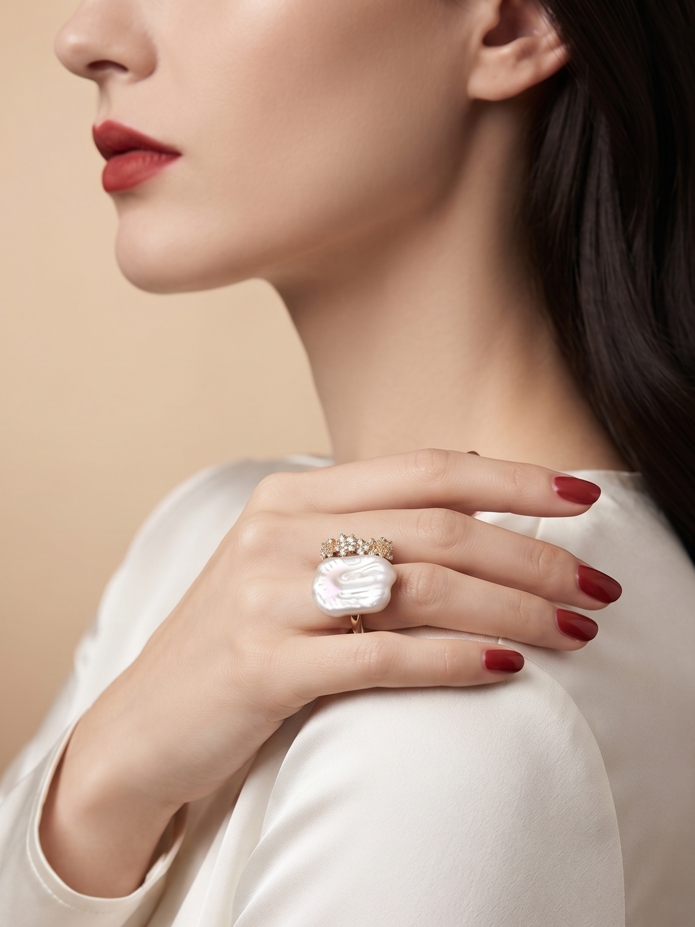 A close-up of a woman wearing a large white sculptural ring with a gold band, resting her hand on her shoulder against a warm beige background.