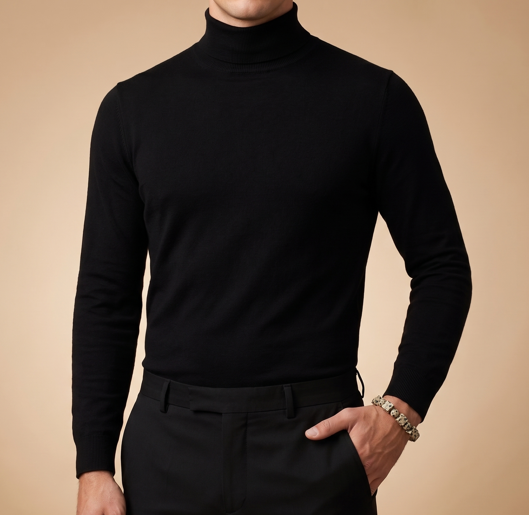 A man wearing a black long-sleeve mock neck turtleneck sweater and black trousers, standing against a solid beige background.