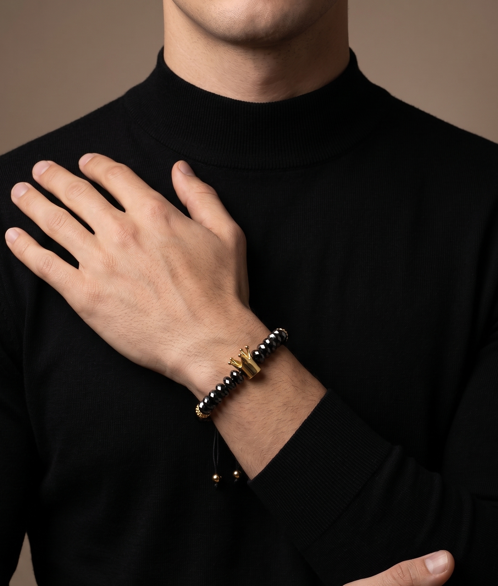 A close-up of a man wearing a black turtleneck sweater, showcasing a black beaded bracelet with a gold cross charm on his wrist.