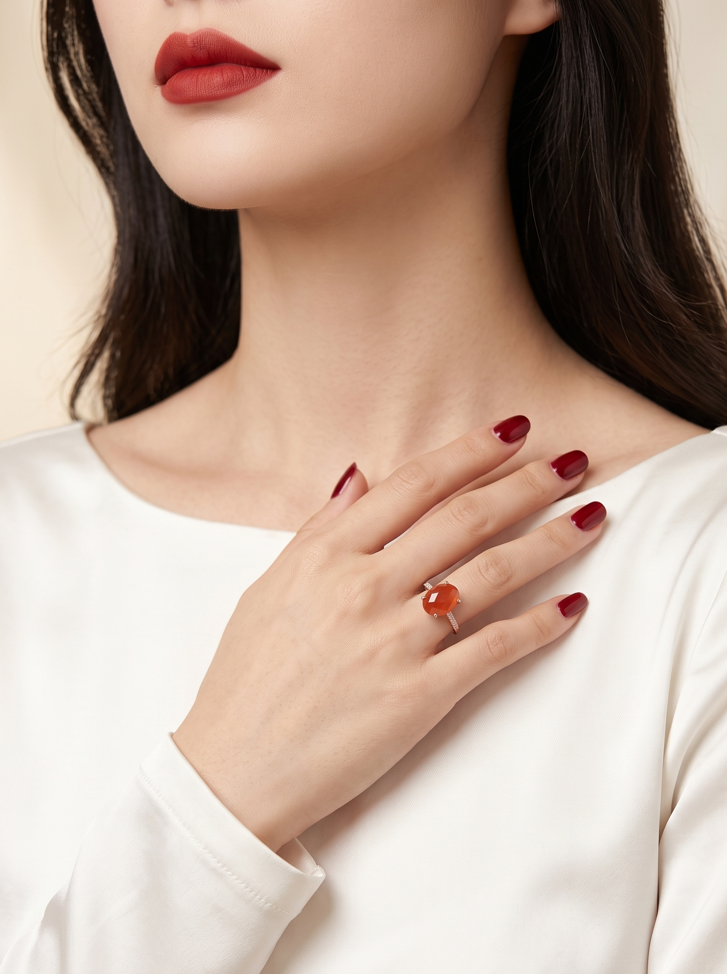 A close-up lifestyle shot of a woman wearing a silver ring with a round orange cabochon stone, styled with dark red nail polish and a white satin top.