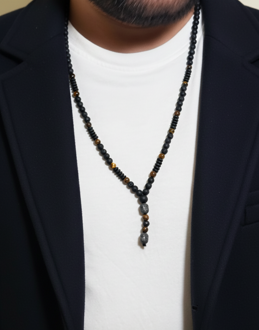 Person wearing a black and brown beaded necklace with a white shirt and dark blazer.
