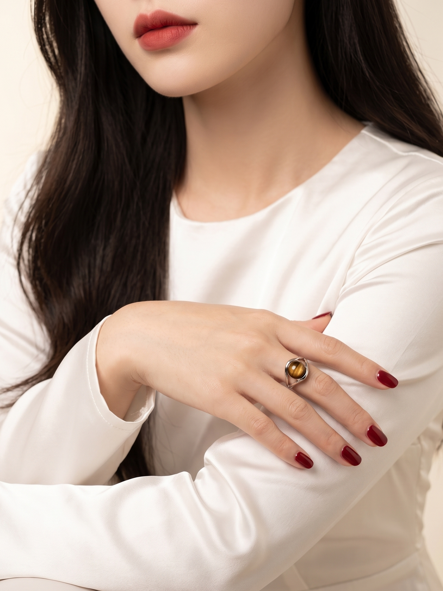A close-up lifestyle shot of a woman wearing a large statement ring with a gold-toned setting and a polished brown gemstone, styled with a white satin dress.
