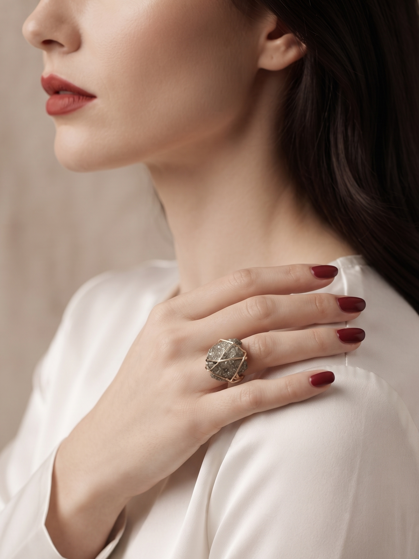 A close-up lifestyle shot of a woman wearing a large, textured silver ring on her finger, dressed in a white satin blouse against a soft beige background.