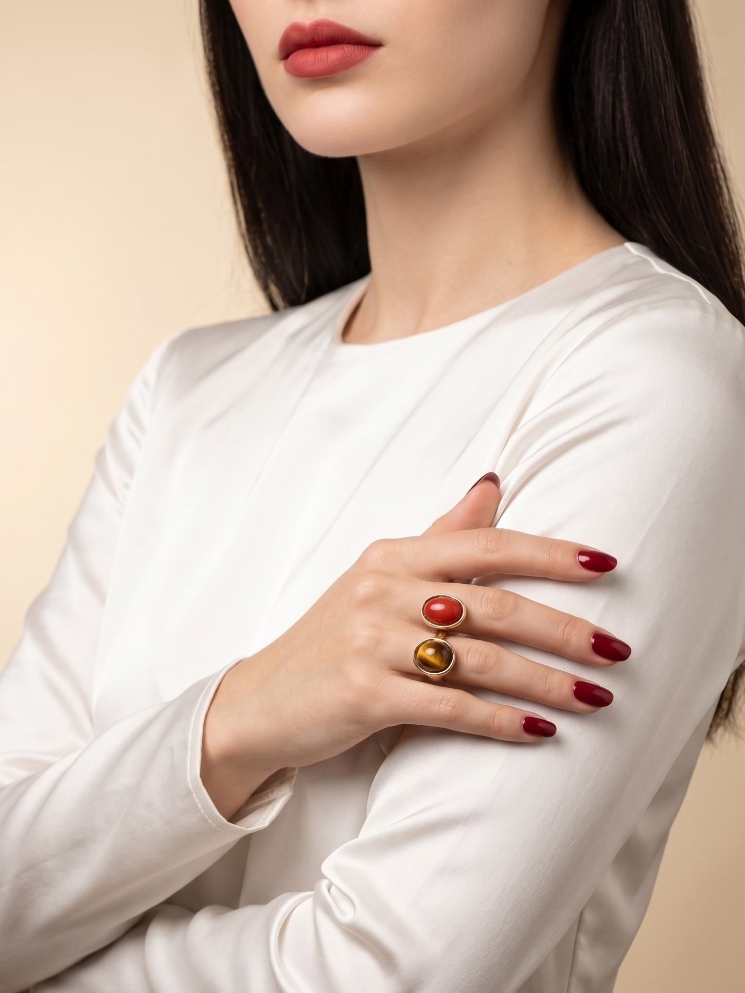 A close-up of a woman wearing two stacked rings on her fingers. The rings feature smooth, polished oval stones in red and gold, set in yellow gold.