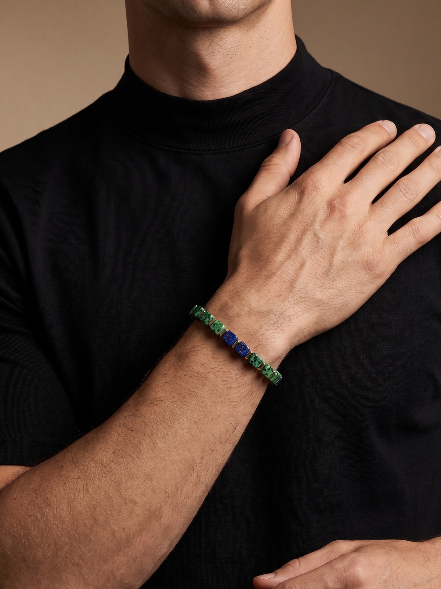 A close-up of a man wearing a black t-shirt, showcasing a beaded bracelet on his wrist. The bracelet features alternating green and blue beads.