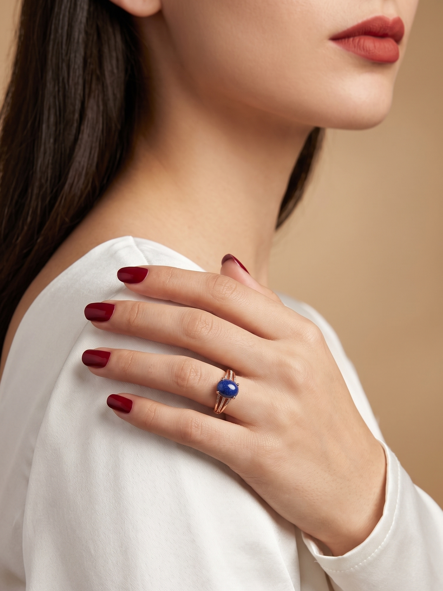 A close-up lifestyle shot of a woman wearing a gold ring with a round blue gemstone, resting her hand on her shoulder.