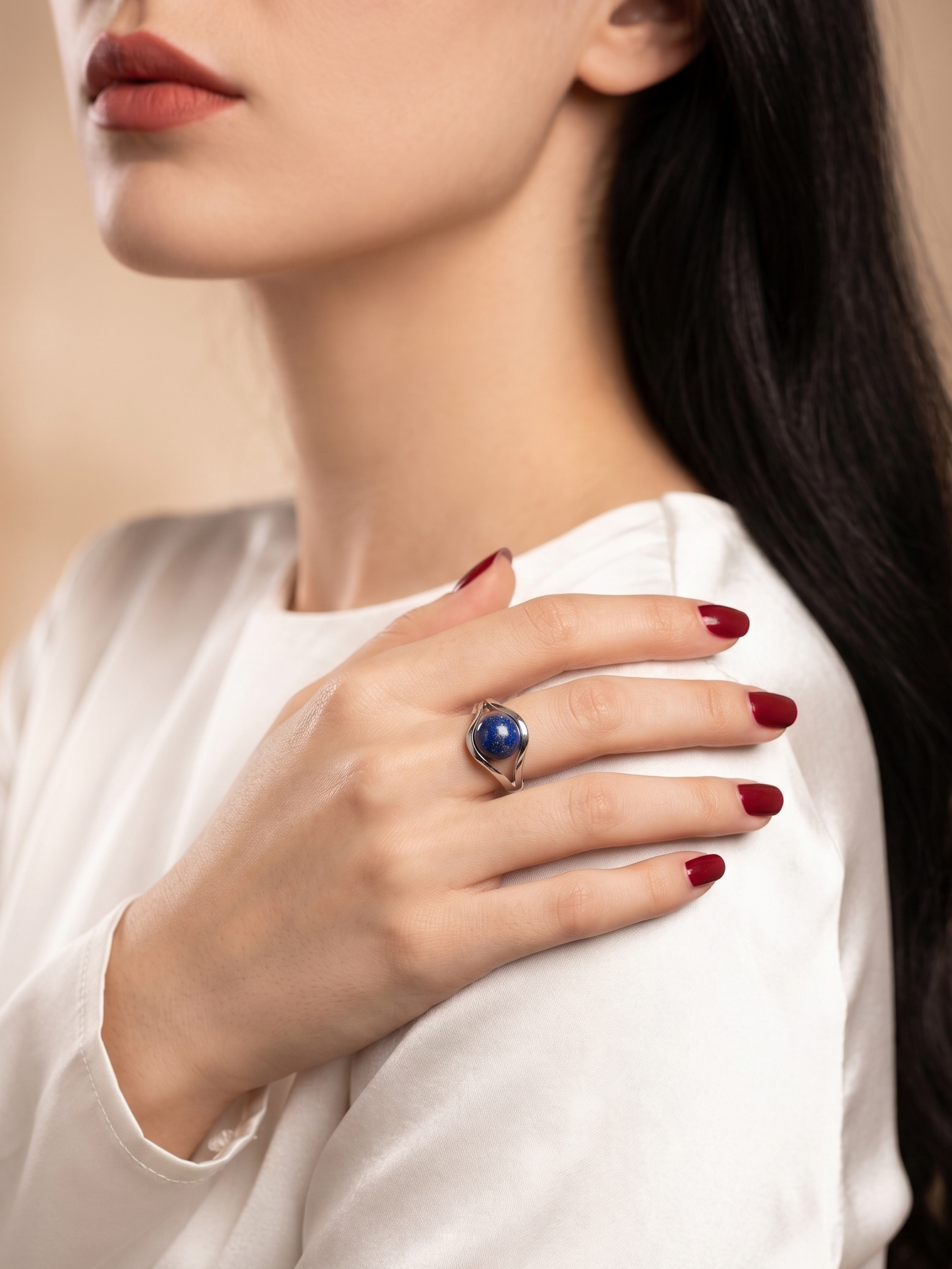 A close-up lifestyle shot of a woman wearing a silver ring with a deep blue oval gemstone, resting on her shoulder.