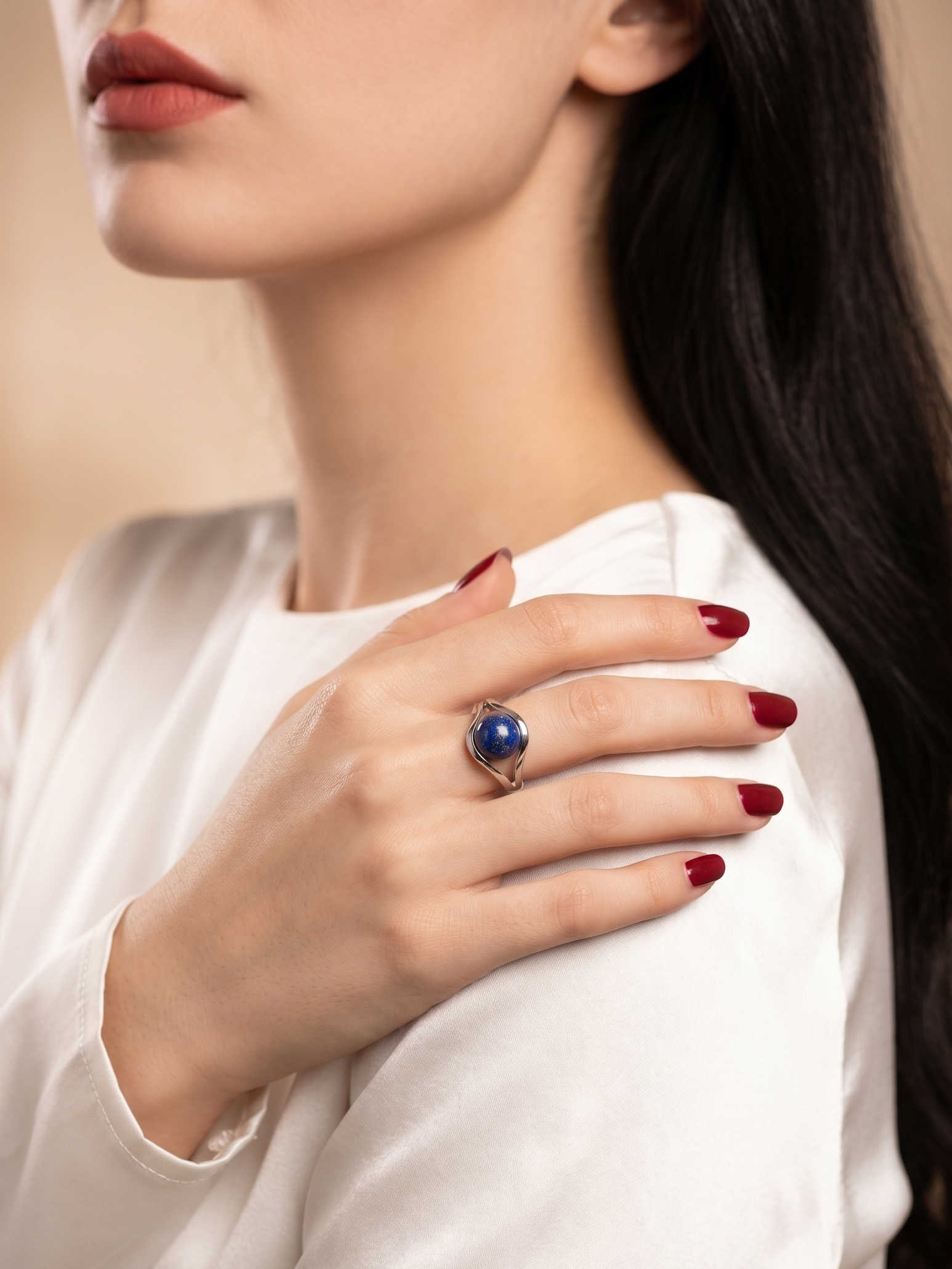 A close-up lifestyle shot of a woman wearing a silver ring with a deep blue oval gemstone, resting on her shoulder.